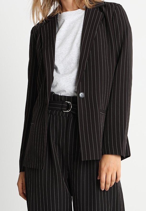 Blazer à rayures noires avec une coupe ajustée, doté d'un col à revers cranté et d'une fermeture à un bouton. Associé à une chemise grise et un pantalon à rayures assorti.