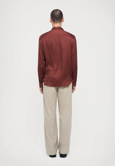 Shirt: maroon, textured, long-sleeved with white polka dots; paired with beige, loose-fitting trousers. Seen from the back.