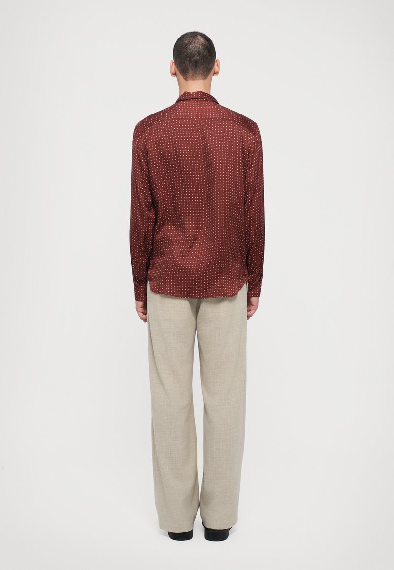 Shirt: kastanjebruin, gestructureerd, langemouwen met witte stippen; gecombineerd met beige, losse broek. Van achter gezien.