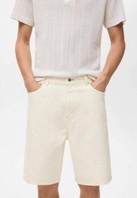 Beige denim shorts med rak skärning, framfickor och subtila sömmar. Stylistiskt ihop med en ljus, texturerad t-shirt med kort ärm.