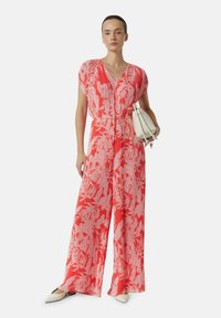 Roter und weißer Blumendruck-Overall mit V-Ausschnitt, kurzen Ärmeln und elastischem Bund, kombiniert mit einer weißen Tasche und spitzen Schuhen.