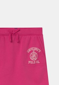 Fuchsiové teplákové kraťasy s elastickým pasem, včetně šňůrky na stažení a předních kapes. Ozdobené bílým vyšitým logem.
