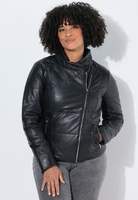 Giubbotto di pelle nera con colletto, cuciture diagonali, chiusura con zip e tasche laterali. Texture liscia con silhouette aderente.