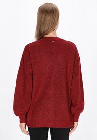 Czerwona swetry z dzianiny o luźnym kroju, z prążkowanymi mankietami i dołem, metalicznymi akcentami oraz okrągłym dekoltem. Teksturowana powierzchnia z błyskami.
