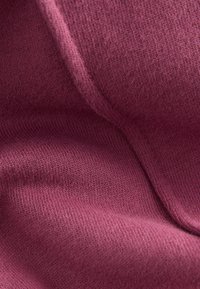 Strikket stof i en dyb mauvefarve, med en blød tekstur, fine syninger og en glat overflade, der viser lette folder og draperinger.