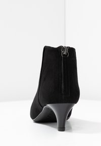 Stivale alla caviglia in suede nero con un tacco basso e una cerniera sul retro. Texture liscia e design slanciato.