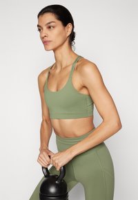 Šviesiai žalios sportinės trumpomis rankovėmis viršutinės dalies su plonomis petnešėlėmis, derančios su aukštu liemeniu leggingais. Modelis laiko juodą kettlebell'ą.