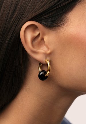 Pendientes de aro dorados con un acento de perla negra lisa. El diseño presenta un acabado brillante y formas circulares, que realzan la elegancia moderna.