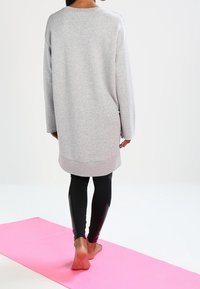 Sudadera gris oversize con mangas largas, combinada con leggings negros con un acento brillante, sobre una esterilla de yoga rosa.