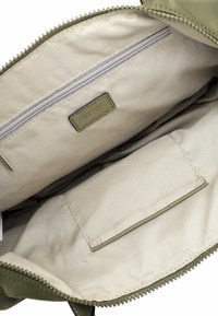 Interno di una borsa verde oliva con fodera beige chiara, dotato di una tasca con zip, un'etichetta e un'ulteriore tasca piatta cucita sul lato.