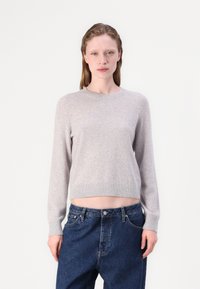 Maglione a maglia grigio chiaro con maniche lunghe e colletto a costine, abbinato a pantaloni in denim blu scuro con una vestibilità comoda.
