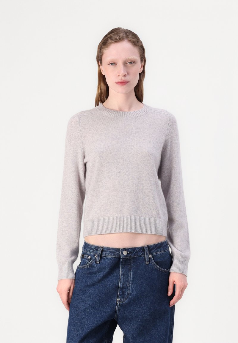 Maglione a maglia grigio chiaro con maniche lunghe e colletto a costine, abbinato a pantaloni in denim blu scuro con una vestibilità comoda.