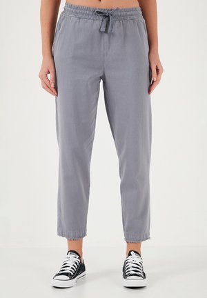 Grijze, lichte, katoenen broek in een mixmateriaal met een elastische tailleband, verstelbare trekkoord en versleten onderranden, gedragen met zwarte sneakers.