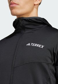Black jacket with a high collar, zippered closure, and textured fabric. Features white "TERREX" logo on the chest and a sleek design.