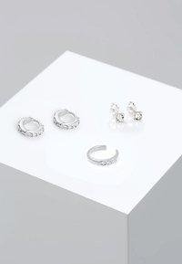 Pendientes de plata con piedras transparentes; se muestran dos estilos de aros y dos estilos de tachuela sobre una superficie blanca. Incluye textura suave y acabado brillante.
