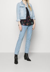 Lyseblå denimjakke, sort blomsterbluse, lyseblå jeans og sorte hælede ankelstøvler. Outfittet har blomsterprint og en afslappet pasform.