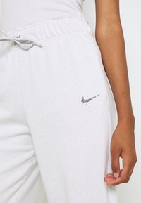 Ljusgrå sweatpants i mjukt material, med ett elastiskt midjeband och snölås samt en liten, flerfärgad Nike-logotyp på sidan.