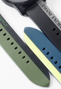 Black watch case with three rubber straps: olive green, navy with lime accent, and solid black—each features multiple holes for adjustment.