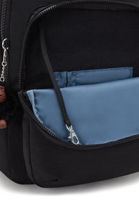 Mochila negra con un compartimento grande y un bolsillo azul desmontable asegurado con una cremallera. Incluye un pequeño charm negro.