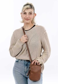 Maglione lavorato a maglia di colore marrone con texture a costine, abbinato a jeans a vita alta blu chiaro. Borsa a tracolla in pelle marrone con dettaglio della cerniera.