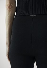 Leggings neri a costine con una vestibilità aderente presentano una cucitura visibile al centro e un piccolo marchio metallico sulla vita.