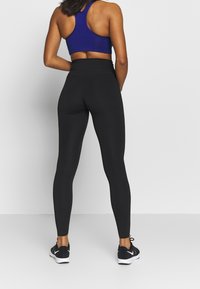 Leggings neri a vita alta in tessuto elasticizzato, abbinati a un reggiseno sportivo con schienale a corsetto blu. Progettati per comfort e mobilità.