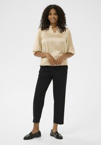 Beige satin bluse med krave, korte ærmer; parret med sorte skræddersyede bukser og sorte loafers. Glat tekstur, ensfarvede.