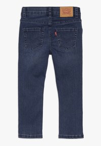 Jeans de mezclilla azul oscuro con un diseño de pierna recta, costuras visibles, dos bolsillos traseros y una etiqueta de parche de cuero en la cintura.