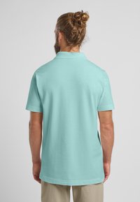 Lichtblauwe polo met een moderne pasvorm, korte mouwen en een klassieke kraag. Gladde textuur, zonder zichtbare patronen of versieringen.