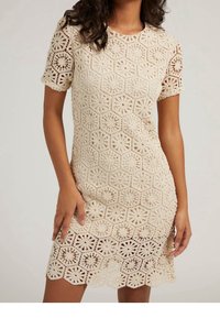Robe en crochet beige clair avec des manches courtes. Présente des motifs hexagonaux et circulaires, un ourlet festonné et une texture ajourée.