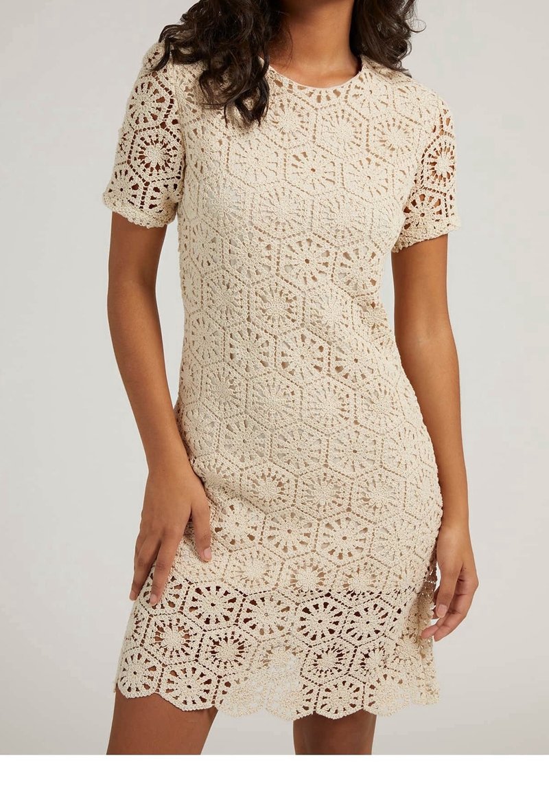 Robe en crochet beige clair avec des manches courtes. Présente des motifs hexagonaux et circulaires, un ourlet festonné et une texture ajourée.
