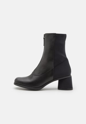 Svarta ankelstövlar med en kombination av läder och tyg. Har en rund tå, dragkedjestängning och en bred blockklack.
