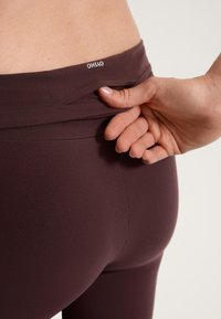 Bordo legice iz raztegljive tkanine, z visokim pasom z logotipom, oprijetim krojem in gladko teksturo.