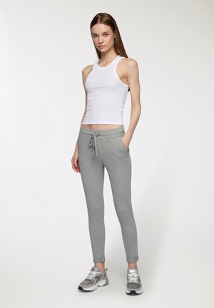 Canottiera bianca senza maniche, pantaloni joggers grigi aderenti con vita elastica e tasche laterali, abbinati a scarpe da ginnastica grigie e argento.