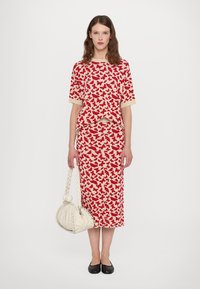 Rood vlinderpatroon co-ord set met een korte mouwen top en een aansluitende rok. Gecombineerd met een witte gevlochten handtas en zwarte flats.
