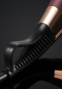 Fer à friser noir et or rose avec poignée ergonomique et grip ventilé reposant sur une surface noire réfléchissante.