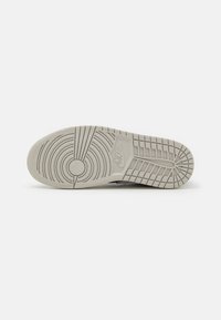 Semelle de basket Nike gris clair avec motifs de bande de roulement circulaires et linéaires, et logo Nike embossé près de la voûte plantaire.