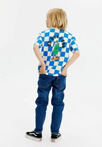 Camisa de manga corta a cuadros azul y blanca con un personaje de spray verde y el texto "oh yes I can", combinada con unos jeans azul oscuro.