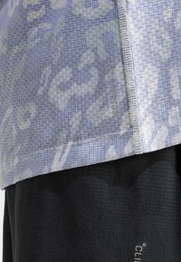 Ljusblå mönstrad topp med en texturerad väv och synliga sömmar, parat med svarta texturerade shorts med en logotyp.