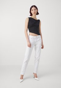 Crni crop top s drapiranim dizajnom i širokim izrezom, uparen s bijelim ravnim trapericama i bijelim cipelama s oštrim vrhom. Minimalistički dizajn i čiste linije.
