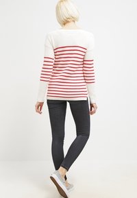 Gestreifter Pullover in Rot und Weiß aus Strickstoff, mit Rundhalsausschnitt und langen Ärmeln, kombiniert mit schwarzen Jeans und grauen Sneakers.