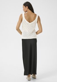Gehaakte tanktop in off-white met gegolfde randen, gecombineerd met een lange zwarte satijnen rok. Glad materiaal en getailleerde pasvorm.