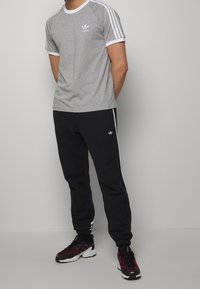 Grijze katoenen t-shirt met witte accenten en drie witte strepen op de mouwen, gecombineerd met zwarte joggingsbroeken met witte zijstrepen en logo.