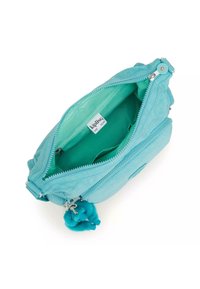 Turkis crossbody taske i blød stof med en lynlåslukning. Indersiden har en lysere grøn foring, flere lommer og en pom-pom nøglering.