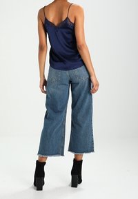 Marinblå satänglinne med spetsdetaljer, matchat med lösa blå denimculotter med fransade fållar. Modellen bär svarta ankelboots.