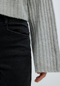 Grau gerippter Strickpullover mit weiten Ärmeln, kombiniert mit dunklen Jeans aus Denim, die über eine Seitentasche und dezente Nähte verfügen.