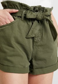 Olijfgroene katoenen shorts met een hoge, ceintuur taille, opgerolde zoom en zijzakken. Kenmerkt zich door een zachte, gestructureerde stof.