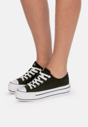 Zapatillas de lona negras con punteras y suelas de goma blanca. Cuentan con cordones blancos y rayas laterales. Diseño de perfil bajo.