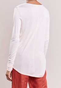 Dlouhý rukáv, světlý růžový shirt s kulatým výstřihem a mírně prodlouženým zadním lemem, vyrobený z měkké, lehké tkaniny.