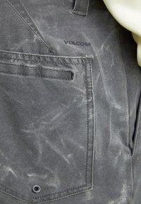 Tissu en denim gris avec une finition délavée, comportant une poche avant et un logo Volcom. Design simple avec des coutures visibles et une texture.